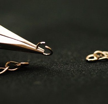 A picture of
							pliers holding a broken gold loop with a chain
						beneath it